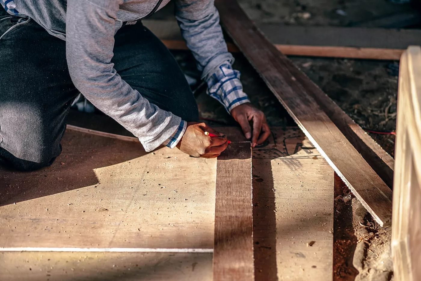 Artisan à genoux qui trace une mesure sur une planche de bois