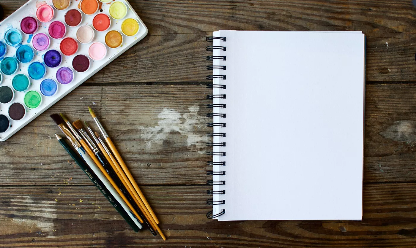 Palette d'aquarelle, pinceaux et carnet vierge sur une table en bois